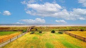 A coastal landscape with a wooden staircase leading to a beach, surrounded by grassy fields and a wooden fence. - Sweet Escape: 2  BR, 2.5  BA House in Crystal Beach, Sleeps 7 (Crystal Beach)