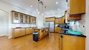 A modern kitchen with wooden cabinets, a central island, bar stools, and a stainless steel refrigerator. - Sweet Escape: 2  BR, 2.5  BA House in Crystal Beach, Sleeps 7 (Crystal Beach)