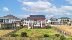 A beachfront property with multiple buildings, including a prominent pink house with a balcony, a light blue building with a covered patio, and a green building with a balcony. - Sweet Escape: 2  BR, 2.5  BA House in Crystal Beach, Sleeps 7 (Crystal Beach)
