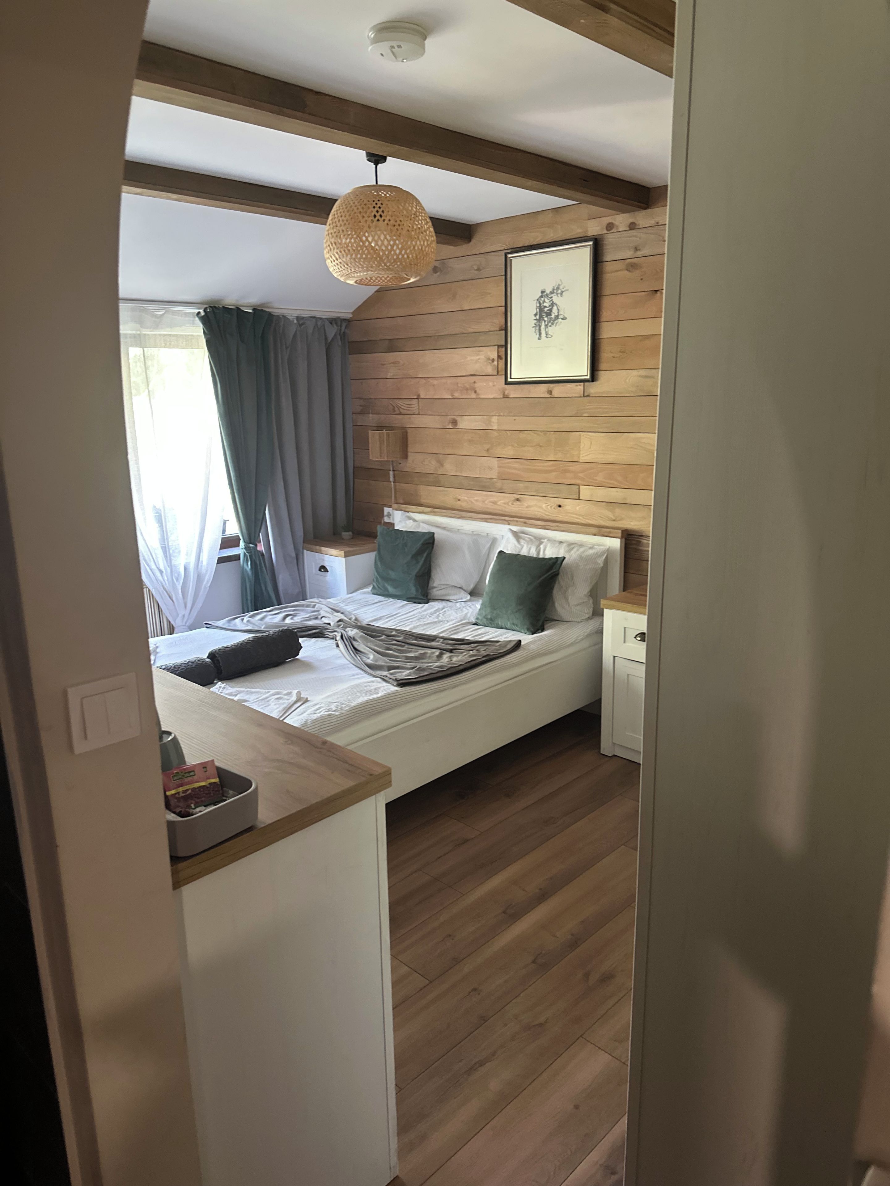Un dormitorio con cabecera de madera, cama con almohadas verdes, mesita de noche y lámpara colgante.