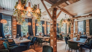 Restaurante com vigas de madeira, plantas penduradas e várias mesas de jantar com cadeiras.