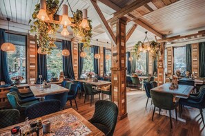 Un restaurante con vigas de madera, plantas colgantes y varias mesas de comedor con sillas.