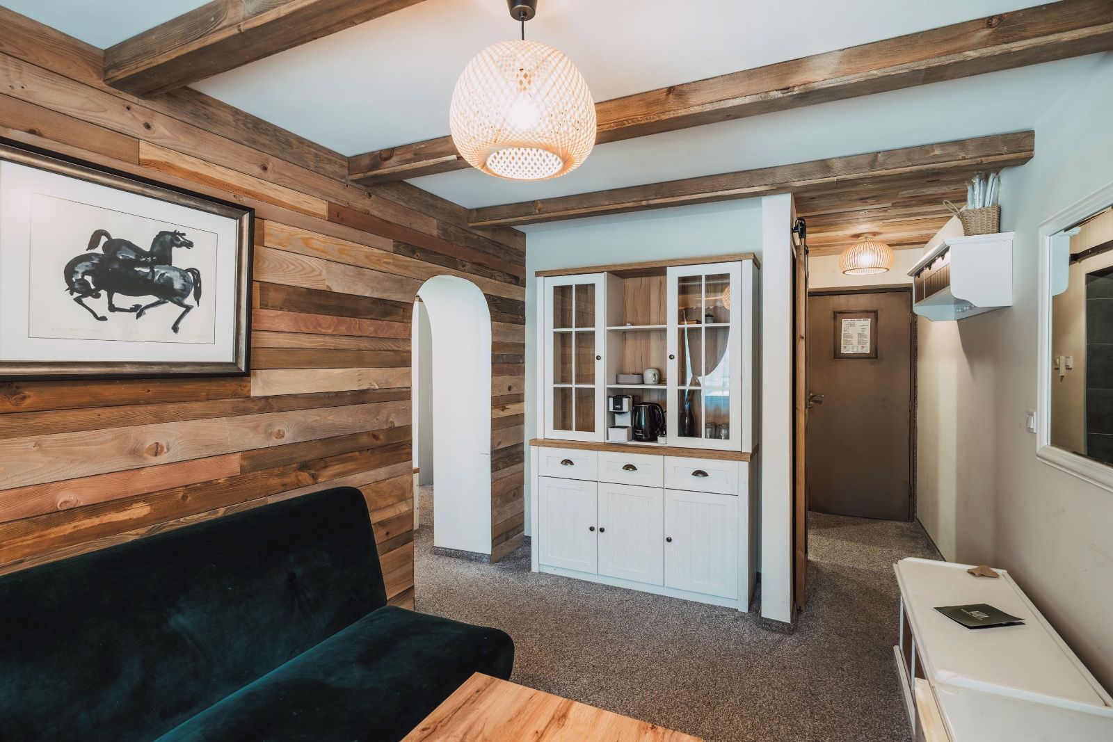 Una habitación con paredes de madera, un sofá negro, un armario blanco con puertas de cristal y una lámpara colgante.