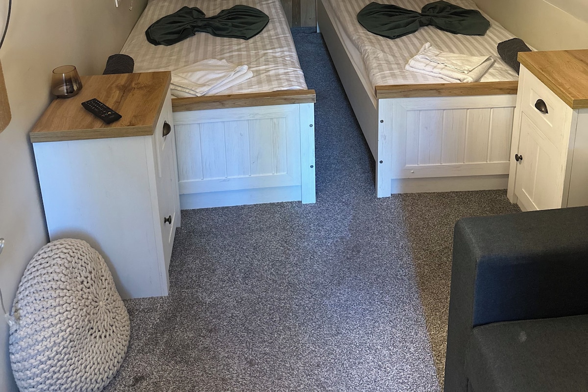 Una habitación pequeña y acogedora con dos camas, un escritorio, una silla y un televisor.
