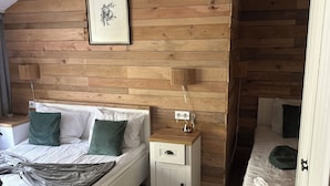 Quarto com parede de madeira, uma cama com almofadas, mesa de cabeceira e luminária suspensa.