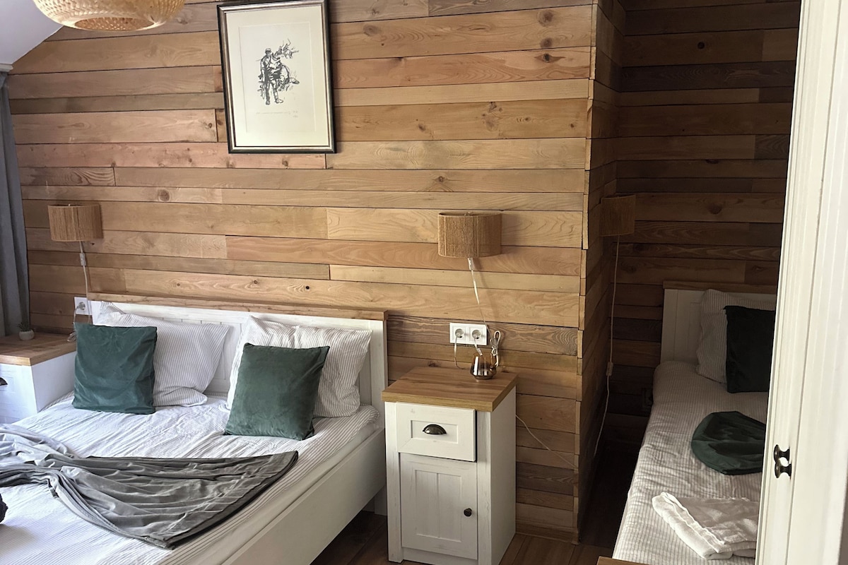 Un dormitorio con una pared de madera, una cama con almohadas, una mesita de noche y una lámpara colgante.