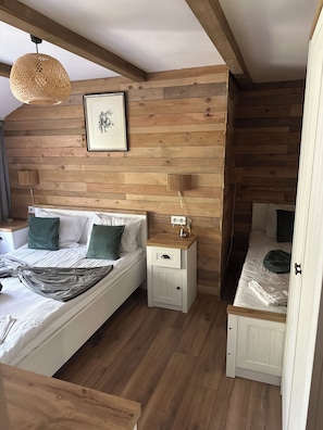 Un dormitorio con una pared de madera, una cama con almohadas, una mesita de noche y una lámpara colgante.