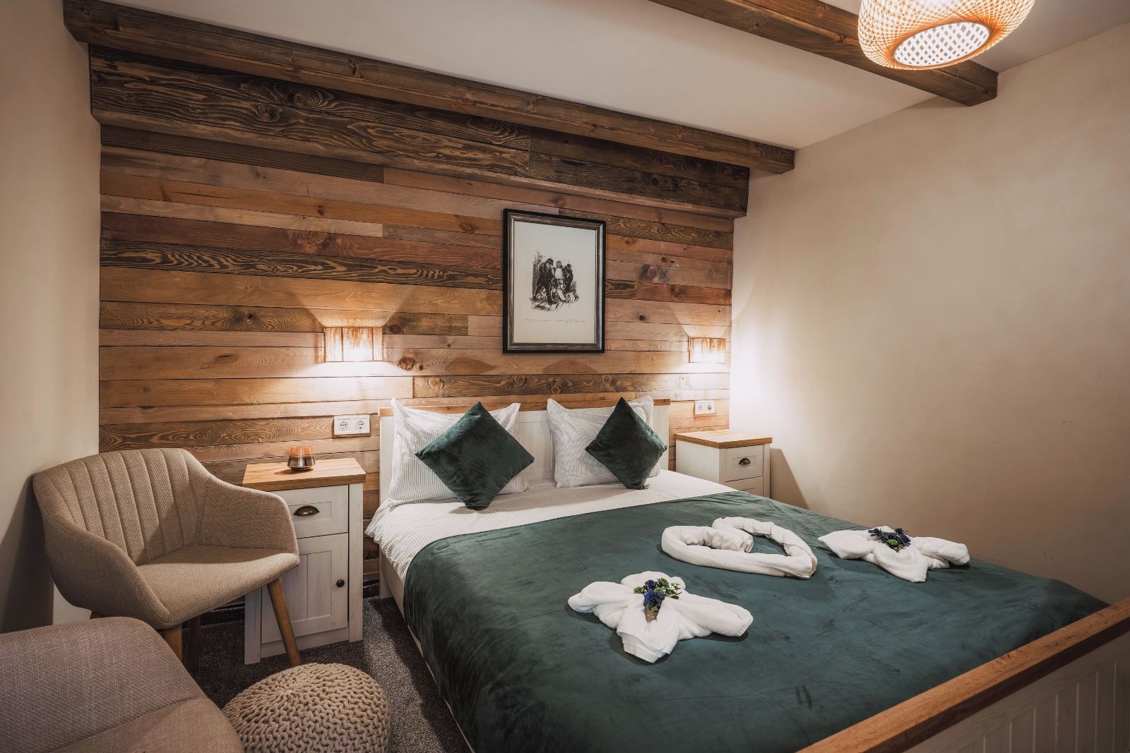 Habitación de hotel con cabecera de madera, cama con ropa de cama verde, dos mesitas de noche con lámparas, una silla y un cuadro en la pared.