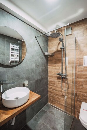 A modern bathroom with a round mirror, a white sink, a shower with a handheld showerhead, and a toilet. - Chalet Evergreen Borovets (Borovets)