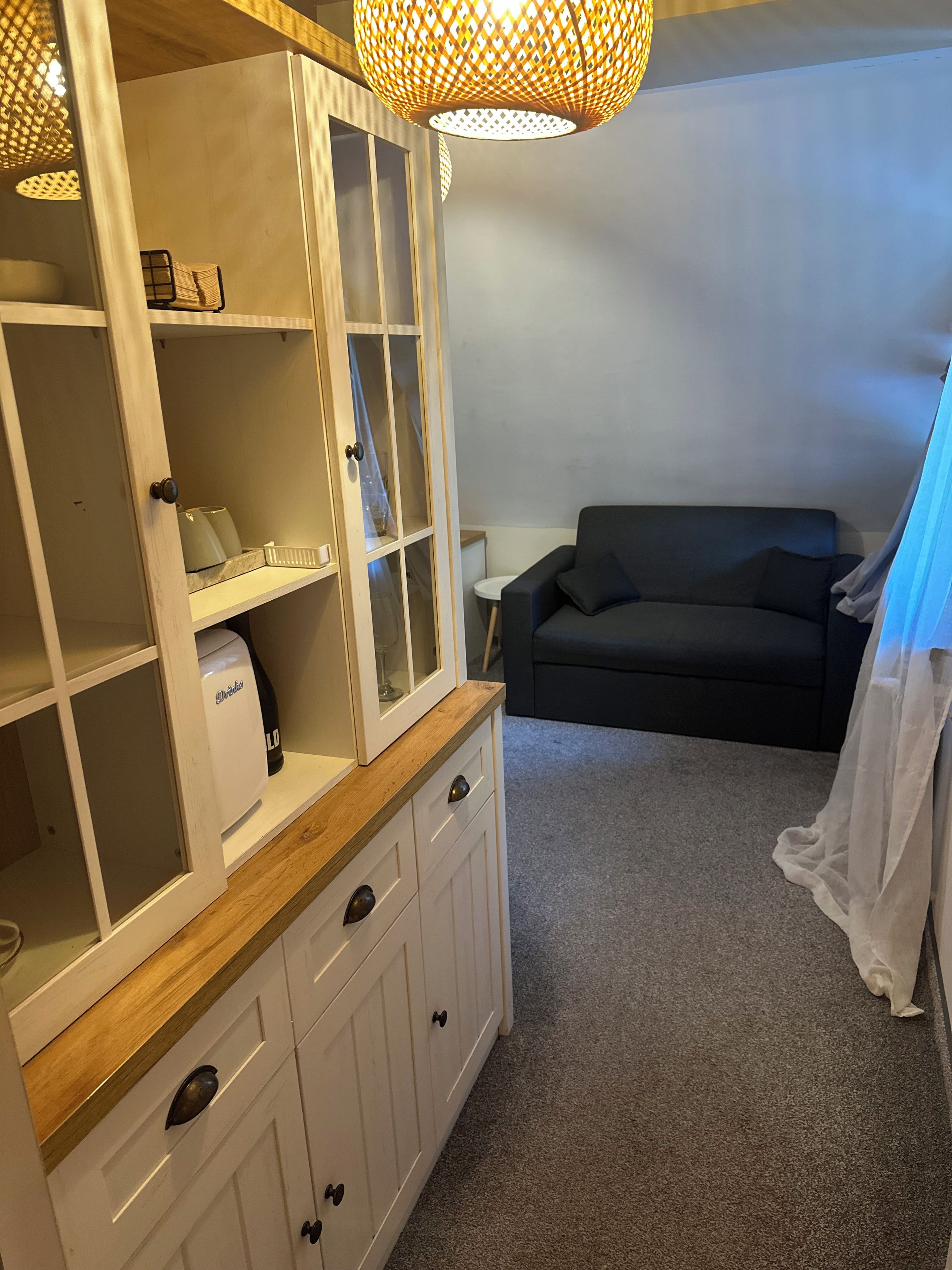 Una habitación con un armario blanco con cajones, un sofá negro y una mesita.