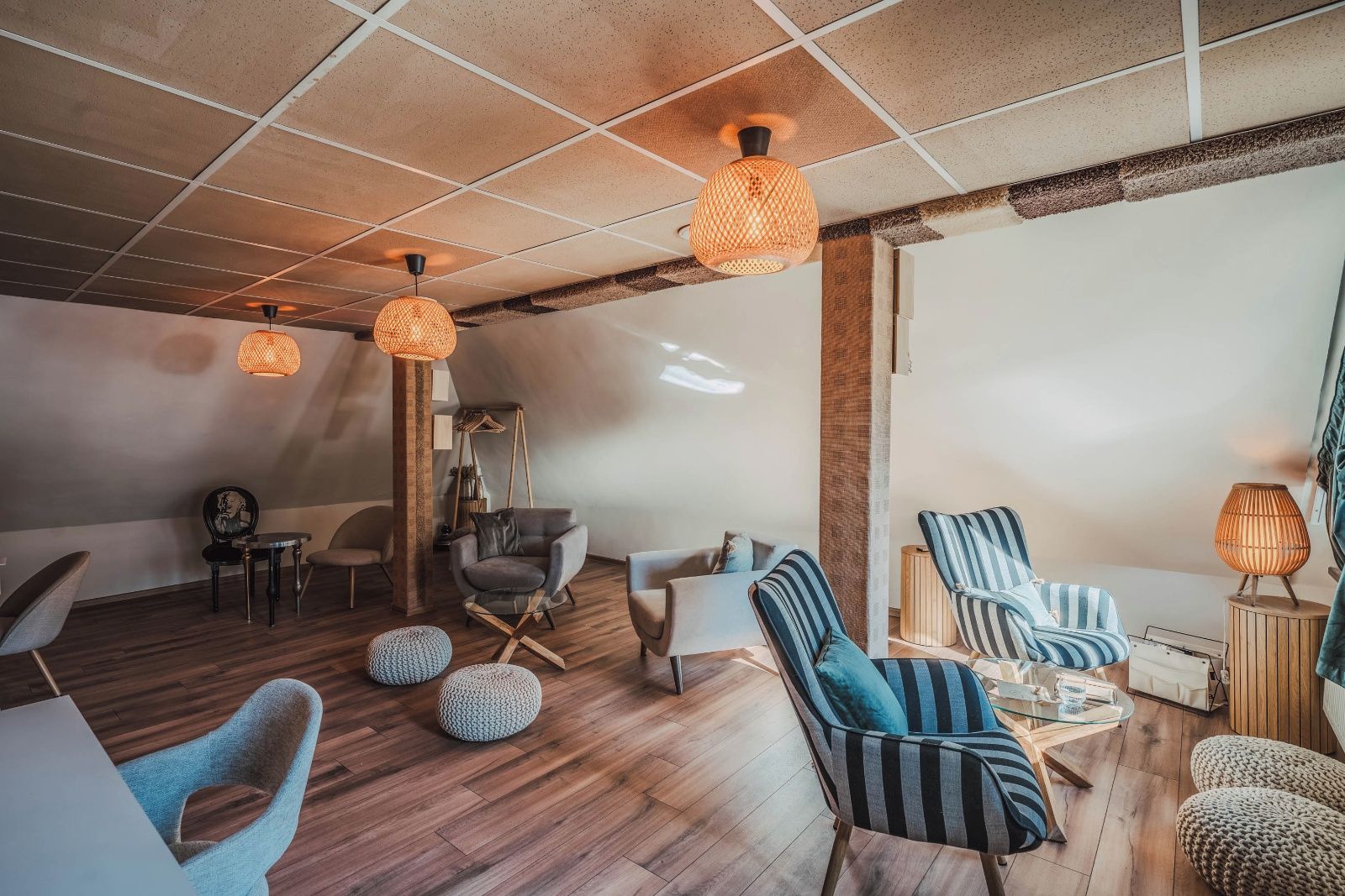 A modern lounge area with wooden flooring, striped sofas, and hanging lamps.