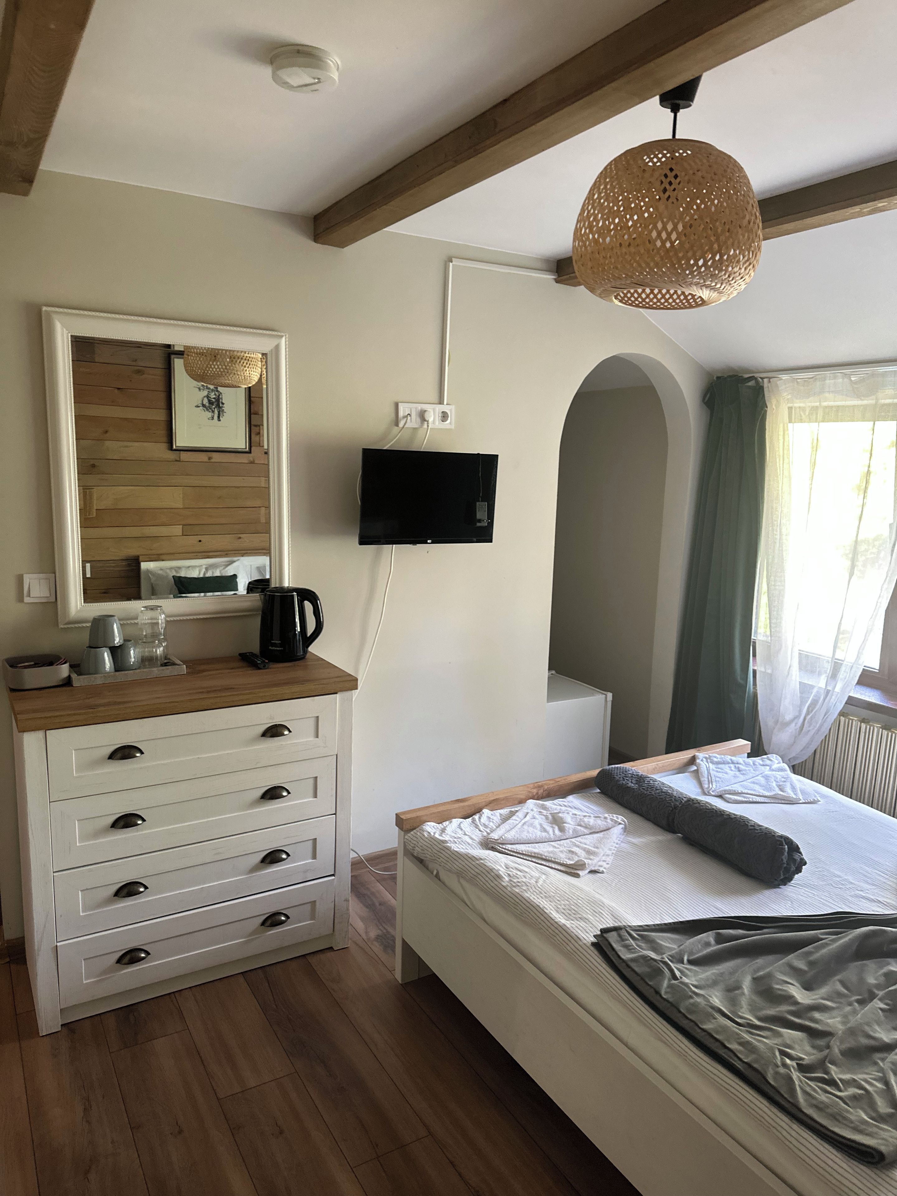 A bedroom with a bed, a dresser, a television mounted on the wall, and a window with curtains.