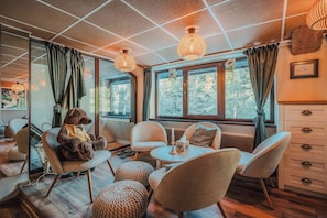 A cozy room with a large window, a teddy bear, and a table with a candle.