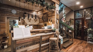 Interior de restaurante com balcão de madeira, banquetas de bar e escada com plantas.