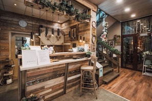 Interior de restaurante con mostrador de madera, taburetes de bar y una escalera con plantas.
