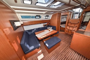 A compact cabin with a sofa, a small table, and a bench. There are windows above the sofa and a control panel on the wall. - Bavaria Cruiser 46 - Paola (Bibinje)