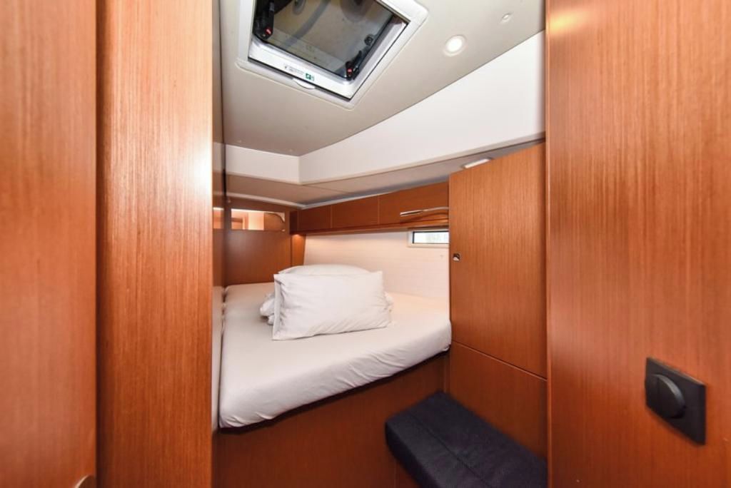 A compact cabin with a single bed, a small bench, and a ceiling-mounted screen.