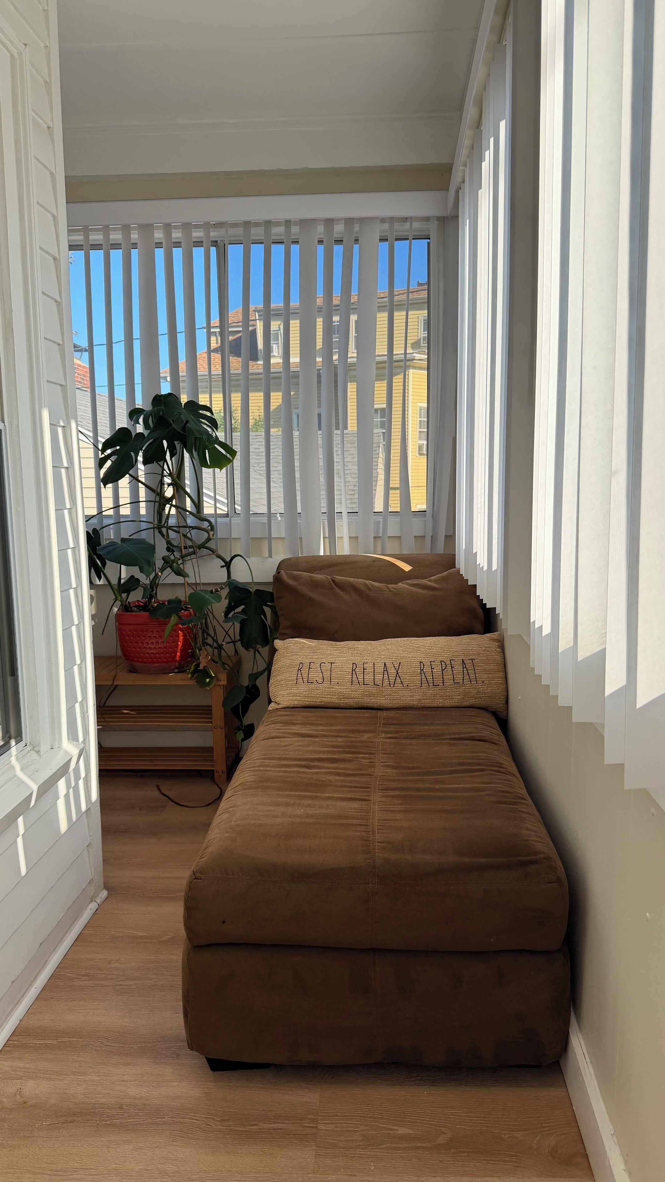 A narrow room with a bench, a potted plant, and a window with blinds.