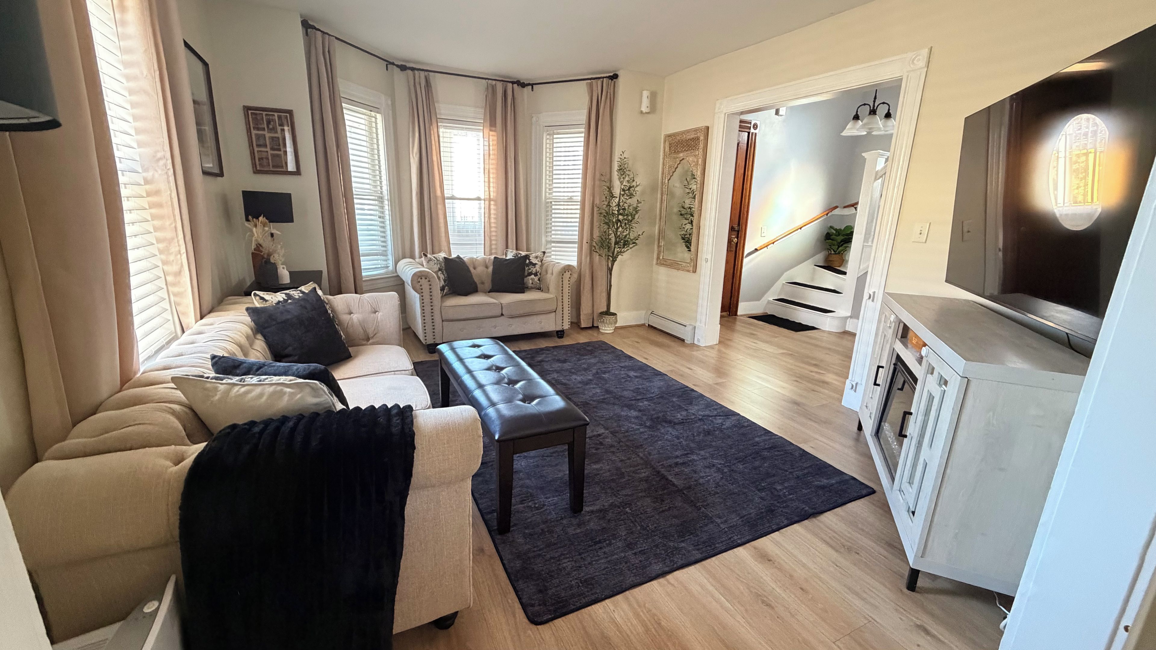 A living room with a sofa, a bench, a TV, and a staircase leading to another room.
