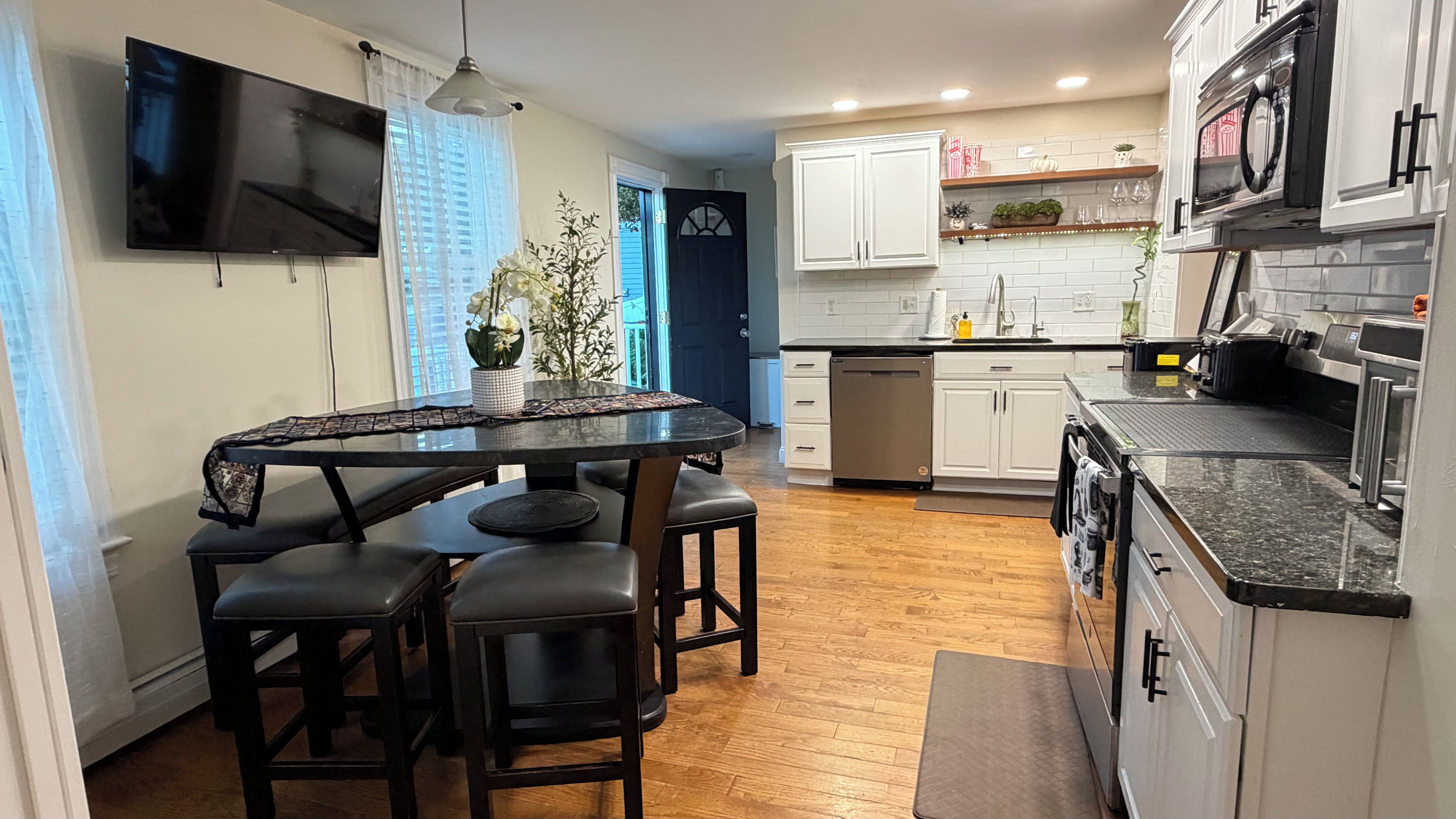 A modern kitchen with white cabinets, a black countertop, and a dining area with a table and chairs.