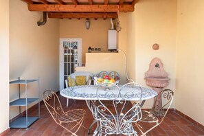 A patio with a round metal table and chairs, a metal shelf, a white door with glass panels, and a pink decorative planter. - Attic Piazza Santa Croce with living terrace (FIRENZE)
