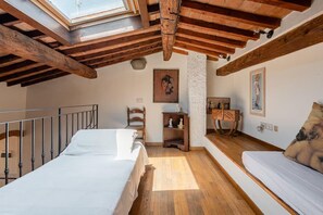 A bedroom with a skylight, wooden beams, a bed, a sofa, a small table, and a chair. - Attic Piazza Santa Croce with living terrace (FIRENZE)