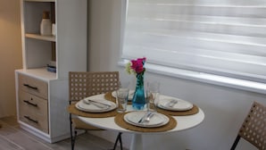 Uma área de jantar com mesa redonda posta para dois, com pratos, talheres e copos.