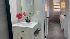 Casa de banho com lavatório branco, espelho e um vaso com flores cor-de-rosa.