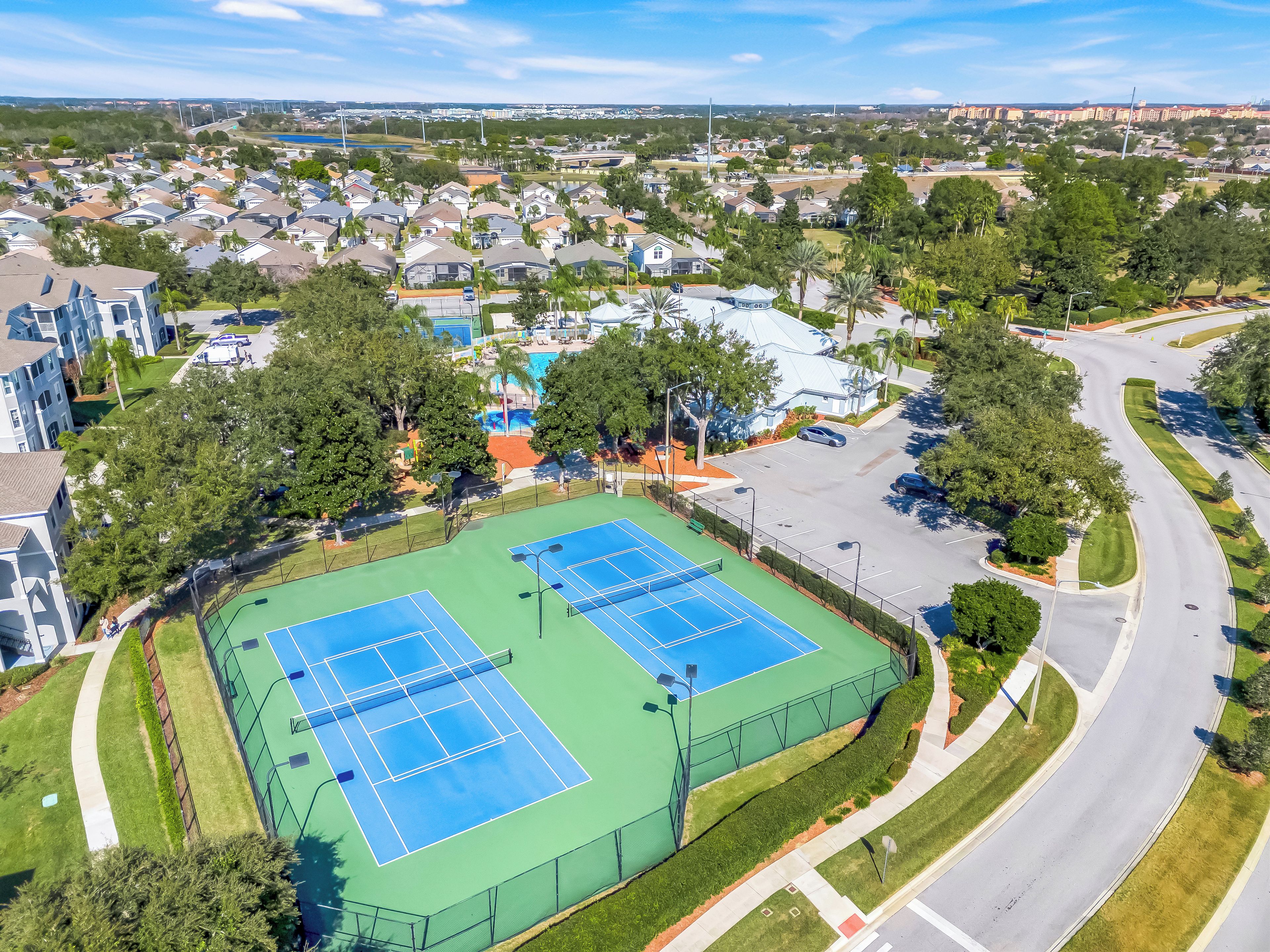 Vista aérea de una zona residencial con dos canchas de tenis, una piscina y una carretera.