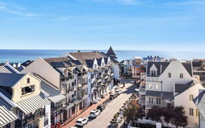 A coastal town with a row of white buildings with black balconies, a paved street, and parked cars. - Southern Yankee | Cozy Rosemary Beach Condo (Rosemary Beach)