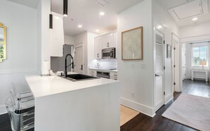 A modern kitchen with white cabinetry, a stainless steel sink, and a built-in microwave. - Southern Yankee | Cozy Rosemary Beach Condo (Rosemary Beach)