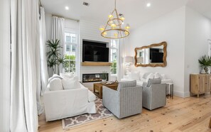 A modern living room with a fireplace, a television, and a large mirror. - Salt and Pine | Golf Cart, Pool, Bikes (Santa Rosa Beach)