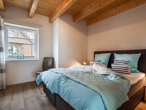 Ein Schlafzimmer mit einem Bett, einem Sessel, einem Fenster und einer Holzbalkendecke.
