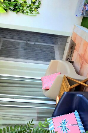 Ein Zimmer mit einem großen Fenster, einem Sessel mit Kissen und einem kleinen Tisch.
