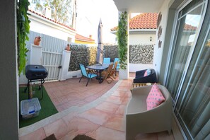 Une terrasse avec un barbecue, une table et des chaises, ainsi qu’un coin salon confortable avec des coussins.