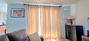 A living room with a sofa, a lamp, a TV, and a window with curtains. - Sunset House Meco pôr do Sol & Praia a 1500 m (Alfarim-sesimbra)