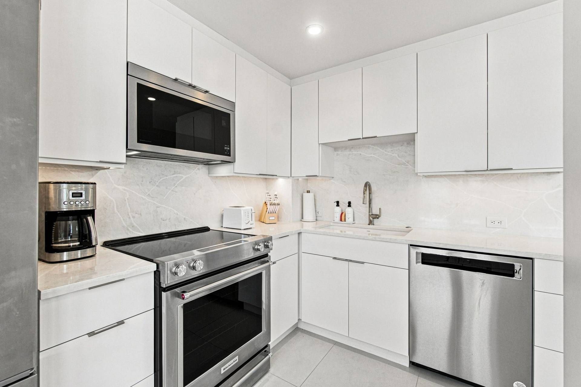 A modern kitchen with stainless steel appliances, white cabinetry, and a built-in microwave.