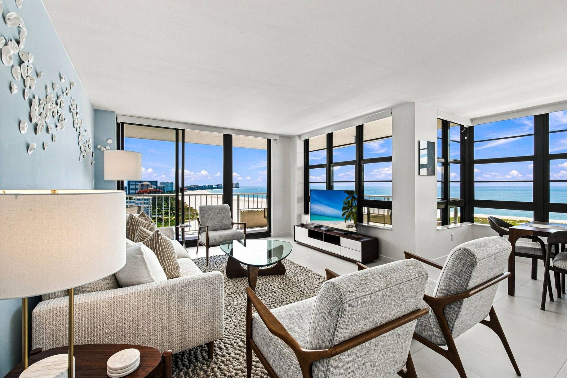 A modern hotel room with a balcony, large windows, and a view of the beach.