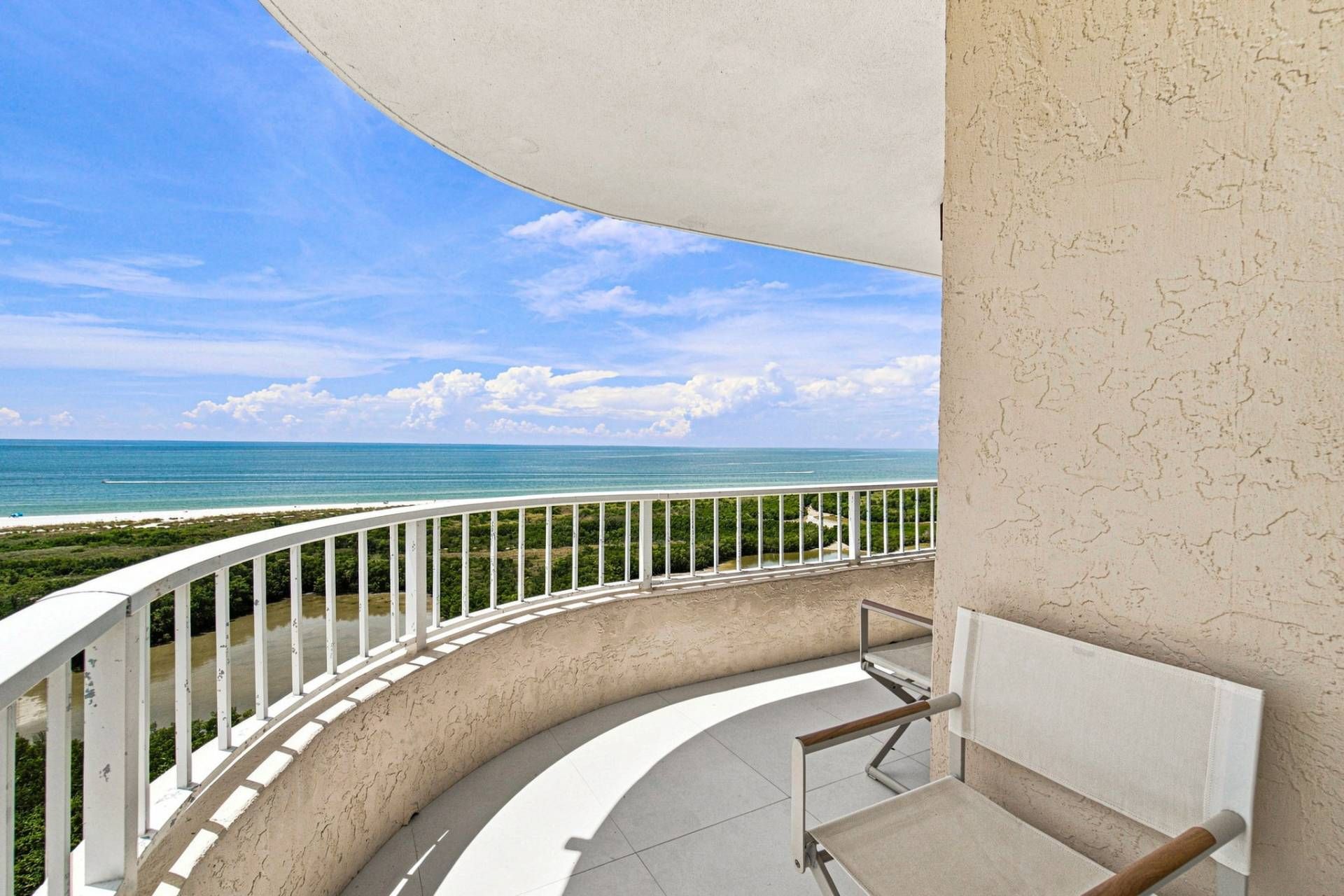 Un balcon doté d’une balustrade incurvée, donnant sur une plage et l’océan.