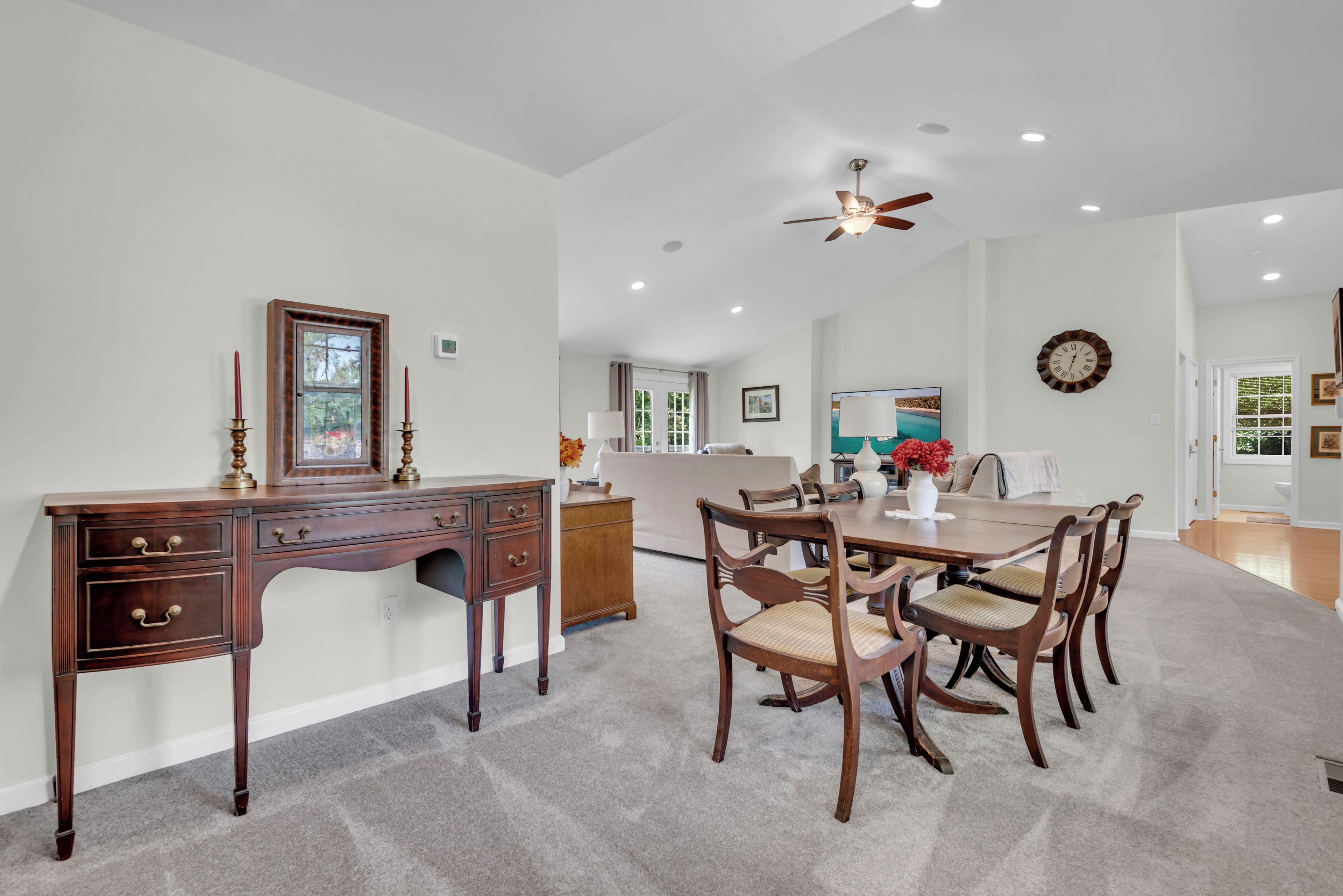 A dining area with a wooden table and chairs, a ceiling fan, and a view of the living room.