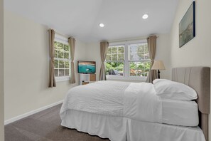 Un dormitorio con cama, televisión y ventanas con cortinas.