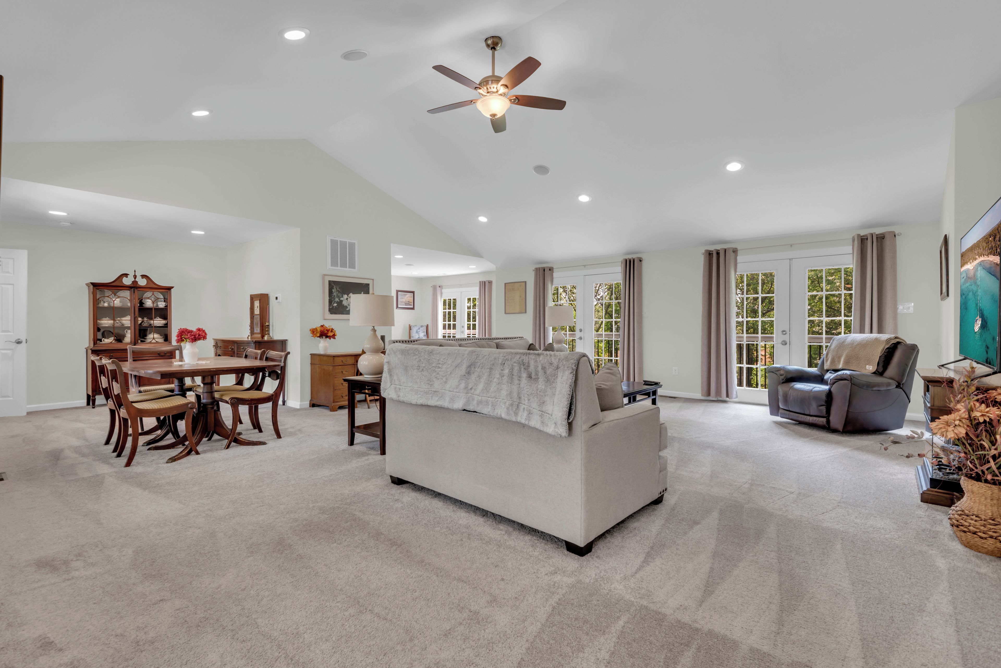 A spacious living room with a high ceiling, a dining area with wooden furniture, and a large window with curtains.