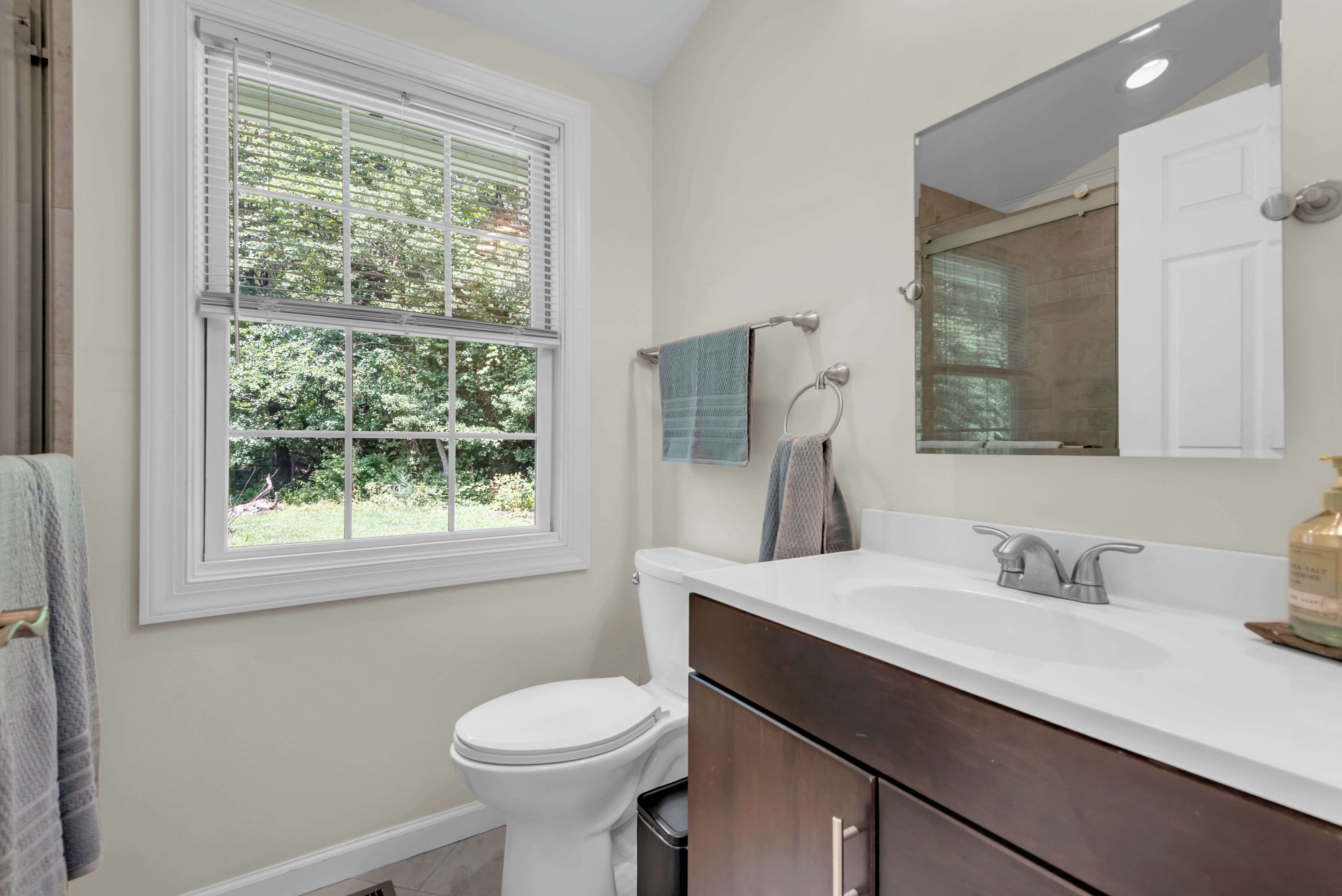 A bathroom with a toilet, a sink, a mirror, and a window.