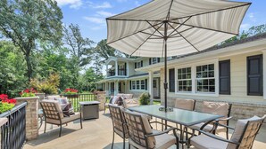 An outdoor patio with a glass table and chairs, a large umbrella, and a house with multiple windows and a balcony. - The Harness Creek Retreat in Annapolis (Annapolis)