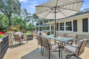 Een terras buiten met een glazen tafel en stoelen, een grote parasol, en een huis met meerdere ramen en een balkon.