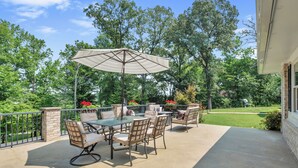 An outdoor patio with a table and chairs, a large umbrella, and a view of a garden and trees. - The Harness Creek Retreat in Annapolis (Annapolis)