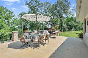 Een terras buiten met een tafel, stoelen, een grote parasol en uitzicht op een tuin en bomen.