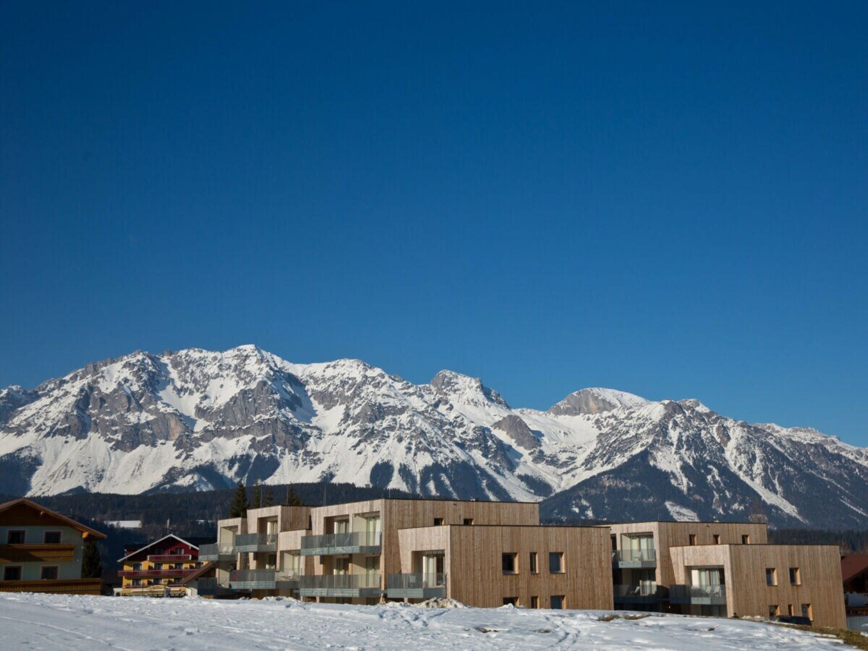 A modern building complex with multiple balconies and a mountain backdrop.