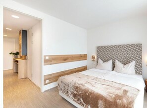 Una habitación de hotel con una cama, mesita de noche y vista al pasillo.