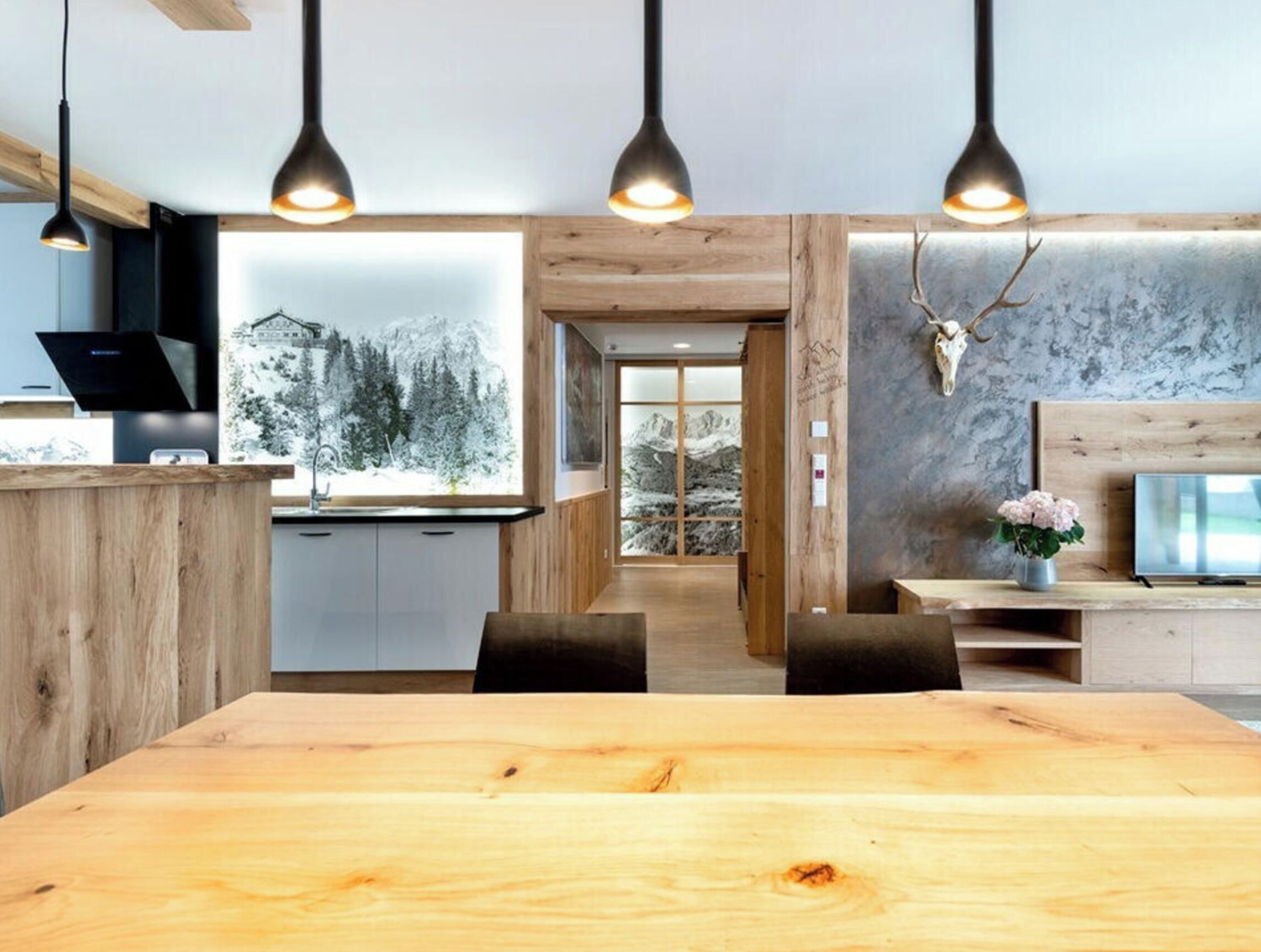 A modern kitchen with wooden cabinets, a dining area with a large wooden table, and pendant lighting.